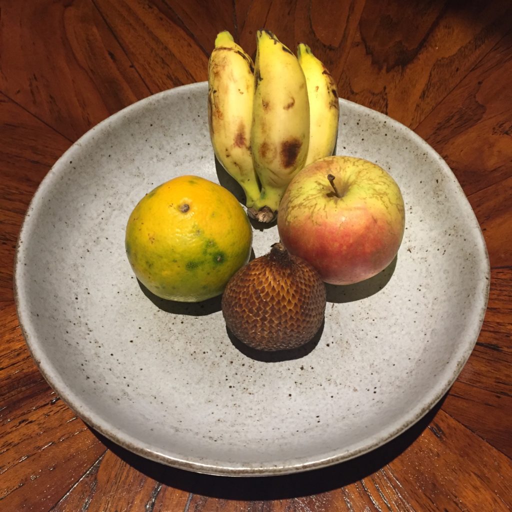 plateau de fruit avec une orange, une pomme, 3 mini bananes et un fruit inconnu
